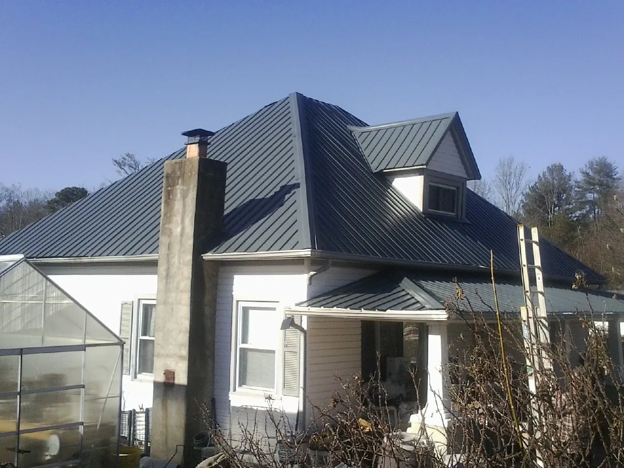 Dark blue standing seam metal roof on a white farmhouse with dormer — Slate & Tile Roof Repair by Roofing Brothers in Deer Lodge
