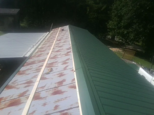 Old rusted panels beside newly installed green metal roofing — Wind Damage Roof Repair by Roofing Brothers in Deer Lodge