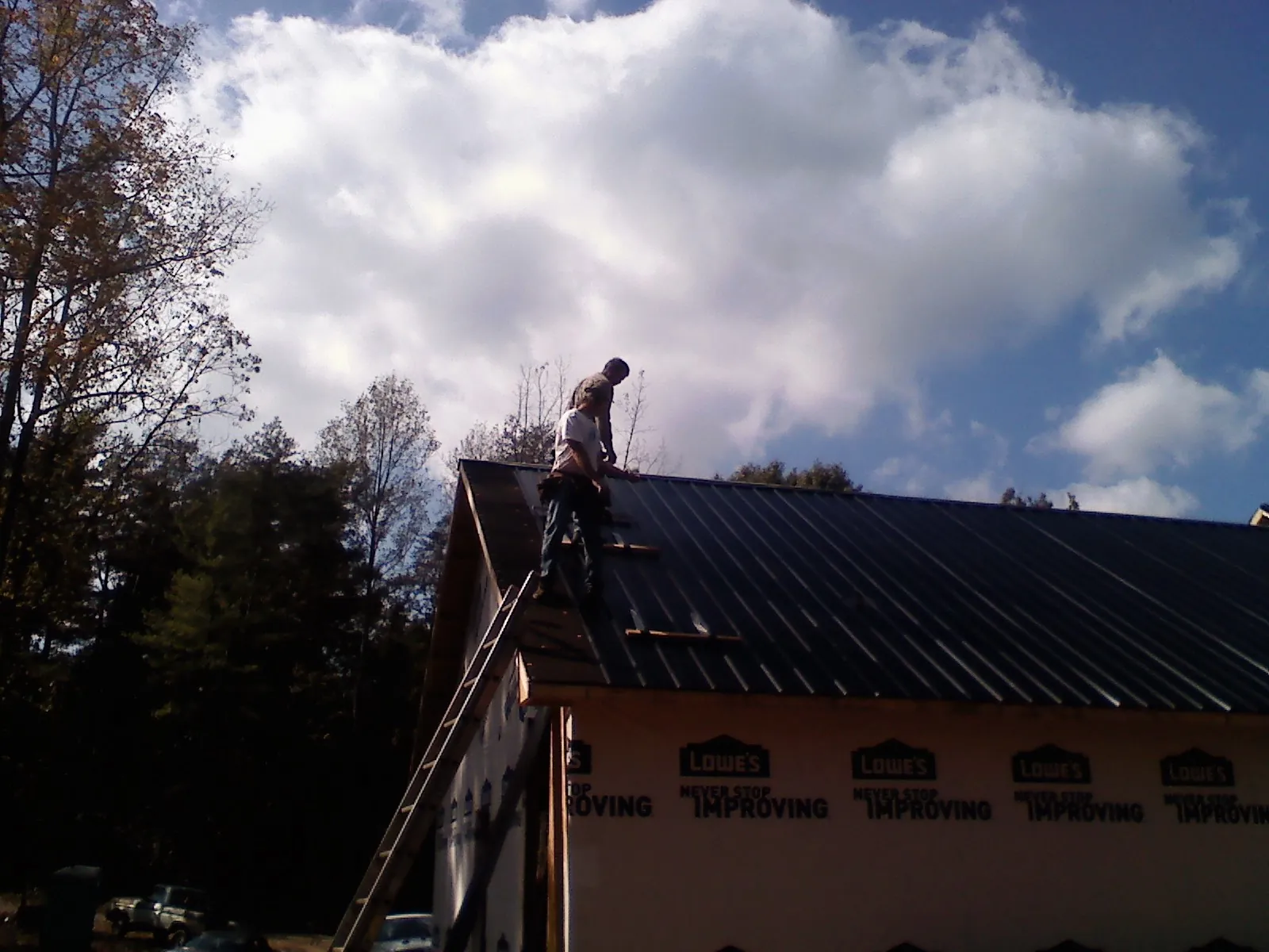 Roofer fastening dark metal panels high against a cloudy sky, from a Roof Inspection job in Deer Lodge