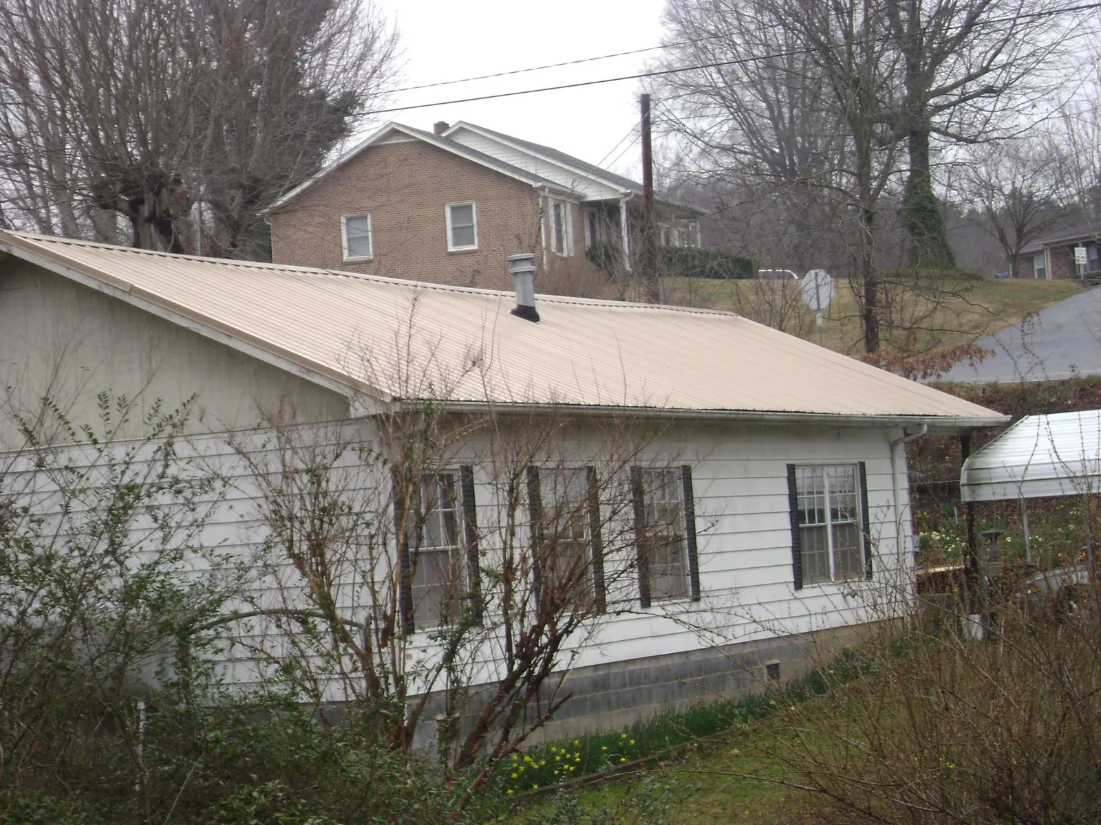 Tan metal roof on a white sided house set into a hillside — Commercial Roofing by Roofing Brothers in Deer Lodge