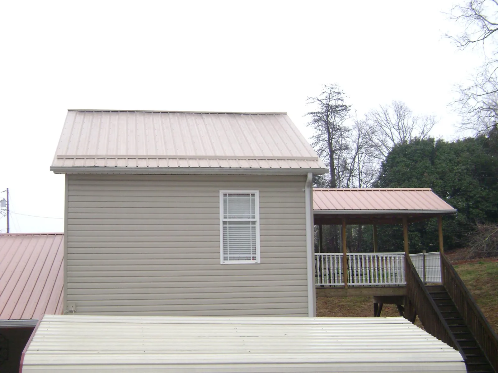 Tan metal roofs on a two story addition and attached porch, from a Roof Replacement job in Deer Lodge